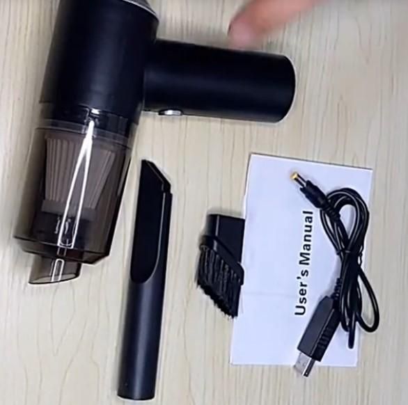 Black handheld vacuum cleaner with attachments and user manual on a light wooden surface