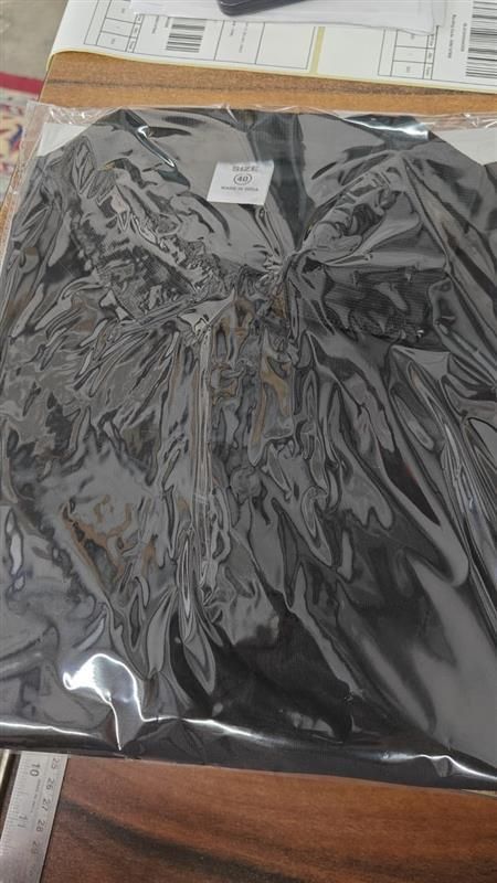 Black lace garment in a clear plastic bag on a wooden surface with a ruler.